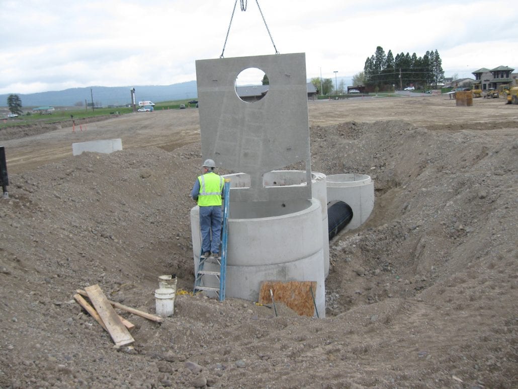 precast concrete storm and sanitary sewer installation in the ground with employee standing on a blue ladder