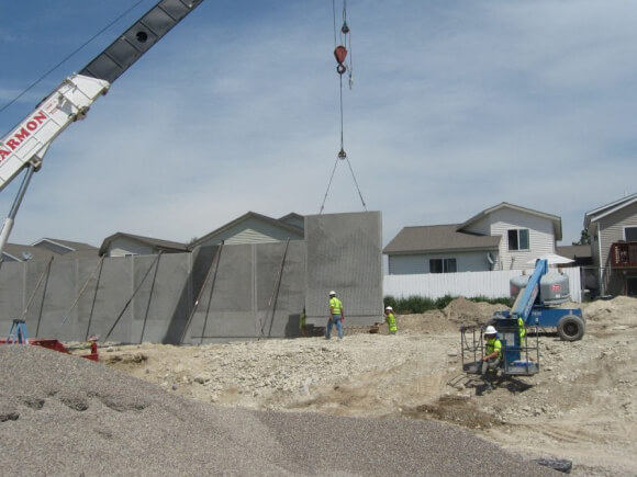 precast concrete panel installation with crane outside home. multiple employees walk on jobsite